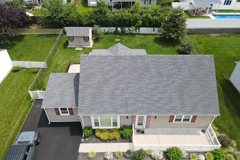 Ranch house with a gray shingle roof seen from above, with a fenced back yard