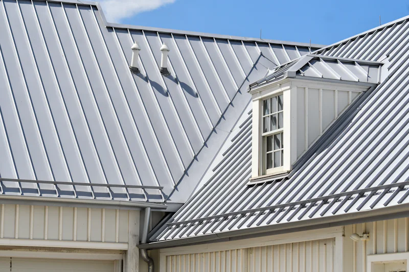 Gray standing-seam metal roof over white siding, with a small dormer